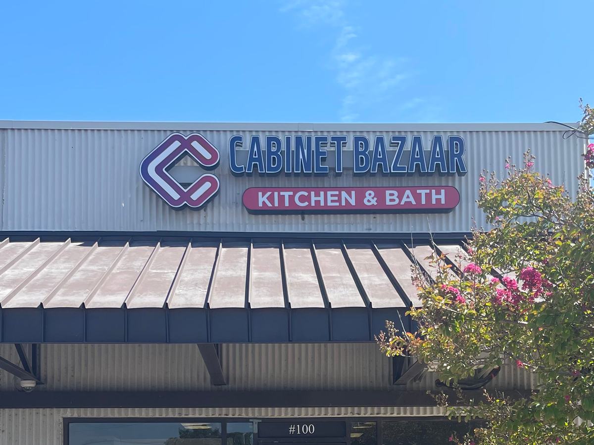 Letrero de Cabinet Bazaar Kitchen & Bath sobre el toldo en 5601 Bandera Rd, Suite 100, con un crespón en flor a la derecha