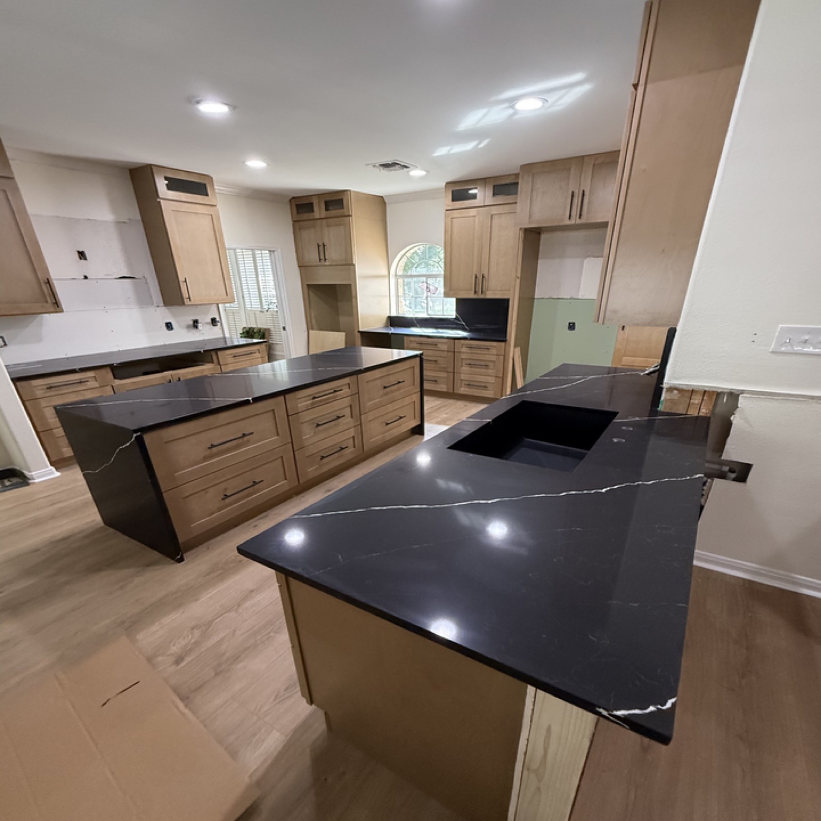 Cocina moderna de arce con isla de cuarzo negro tipo cascada, diseñada e instalada por Cabinet Bazaar en San Antonio