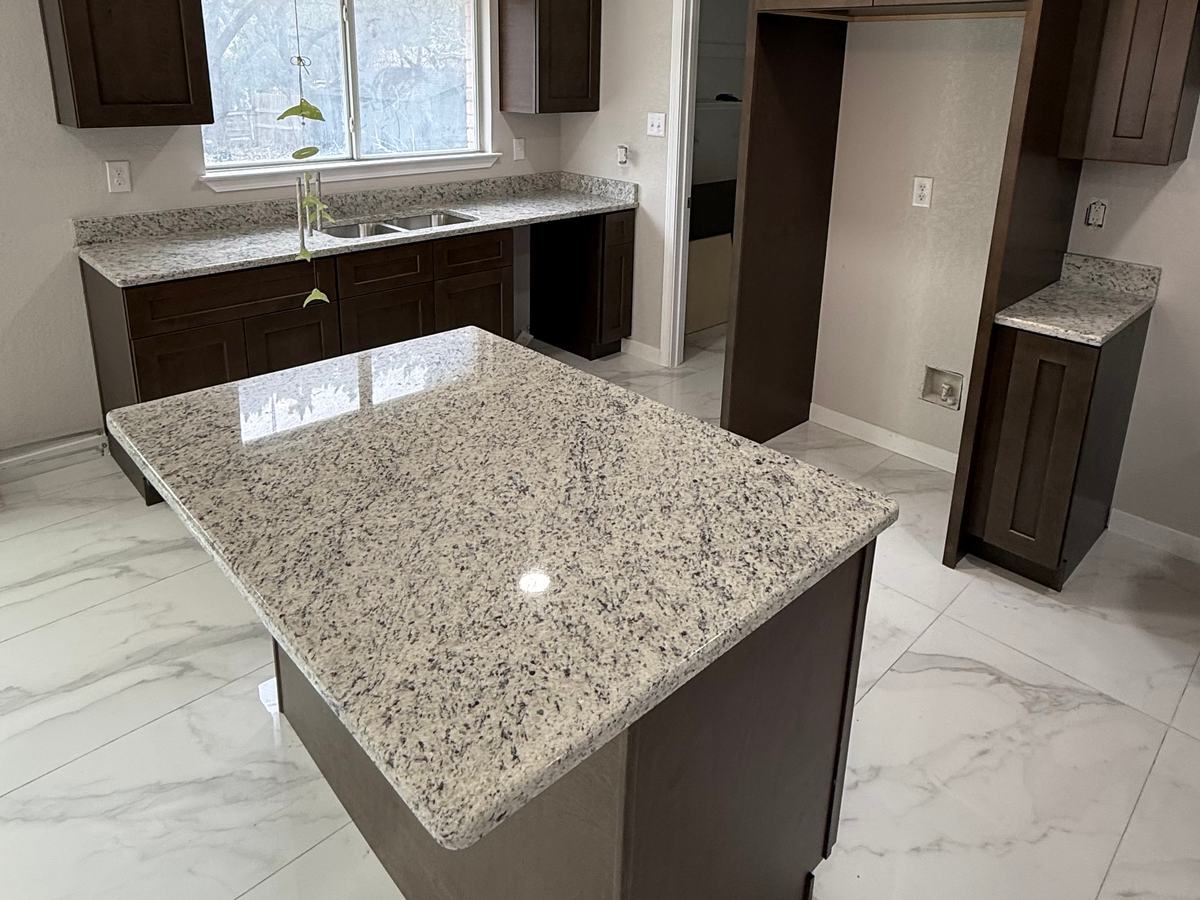 Gabinetes café oscuro estilo Shaker y una isla de granito blanco moteado en una cocina recién instalada con piso de azulejo blanco veteado