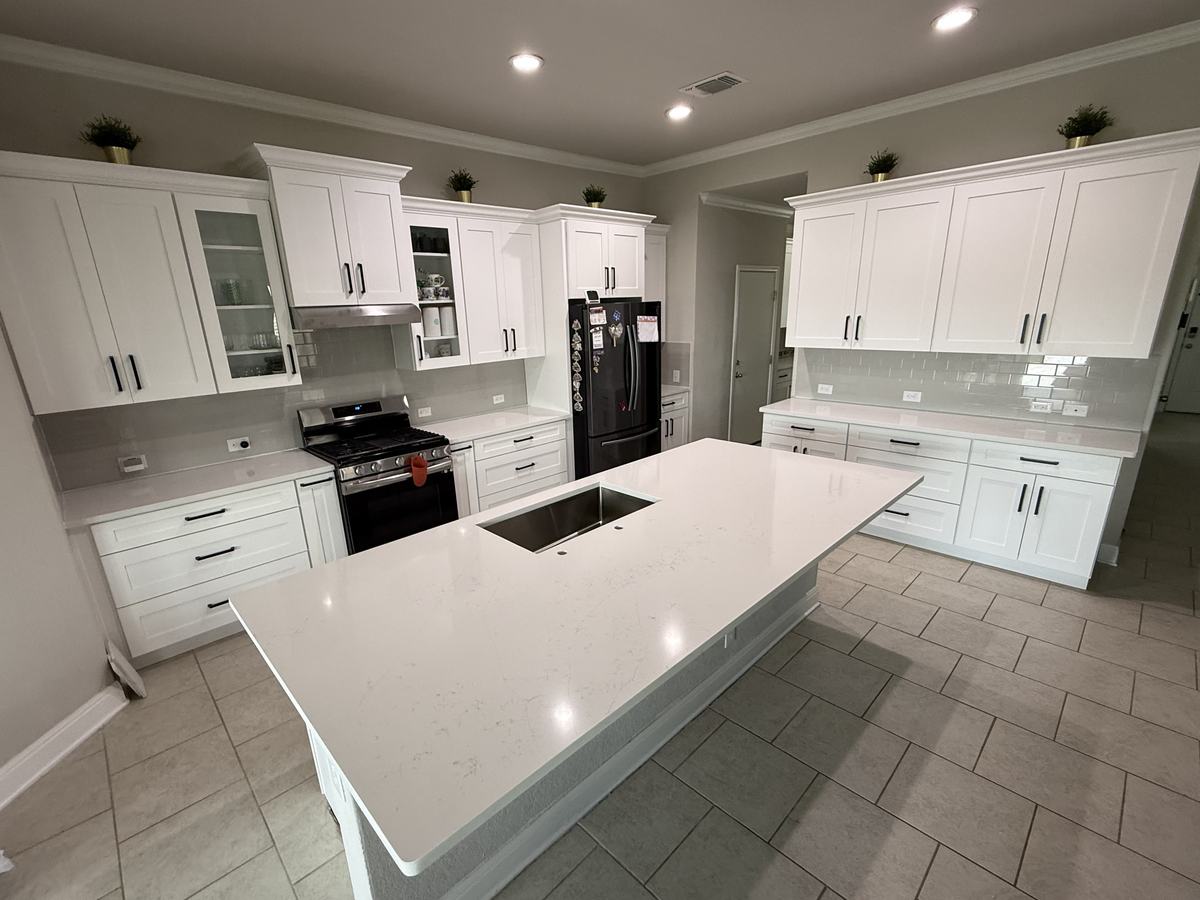 White Shaker-style kitchen with black bar pulls, glass-front upper cabinets and a large white quartz island with an undermount sink