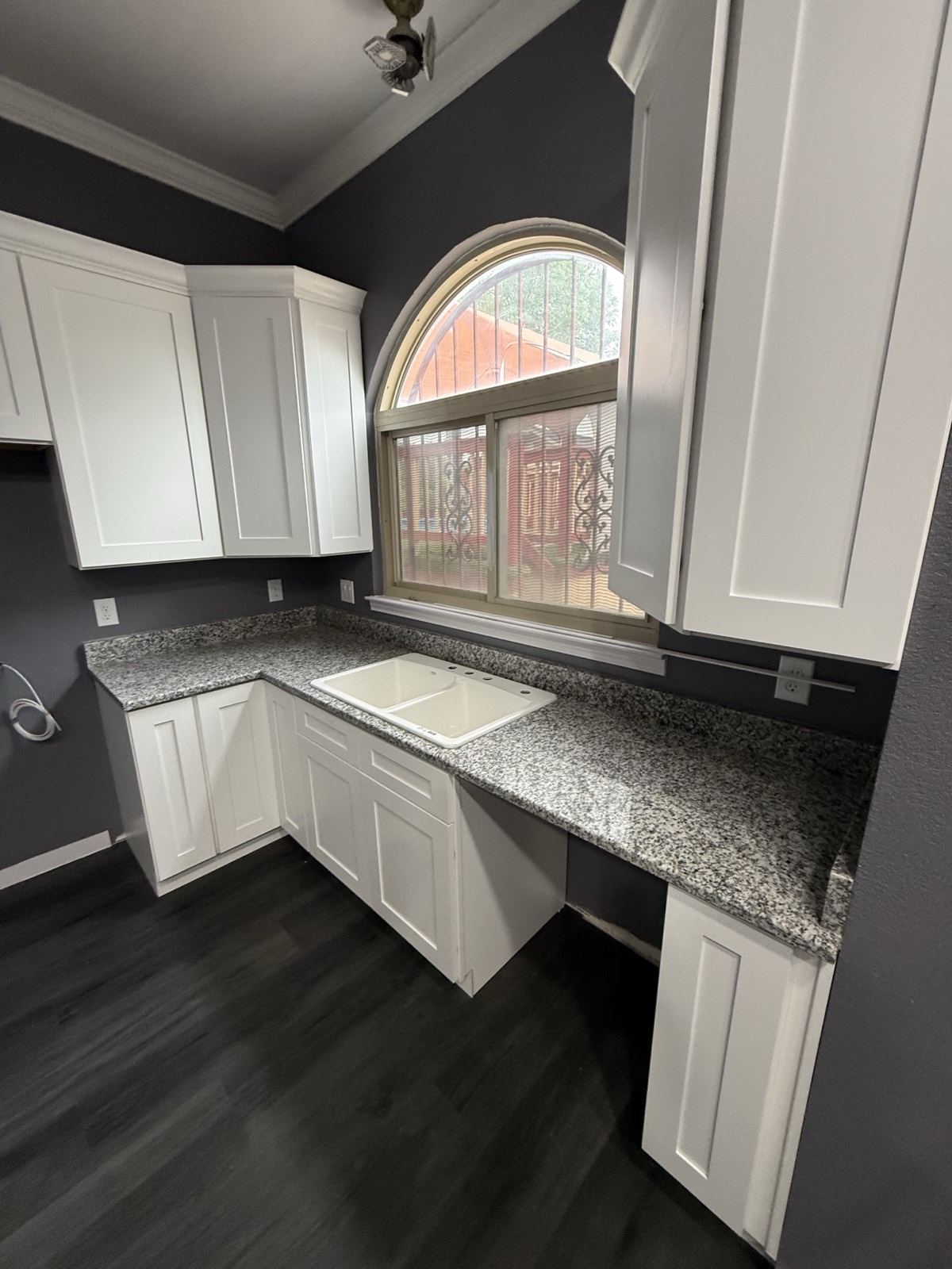 White Shaker-style cabinets around a double sink, with speckled gray granite countertops and an arched window
