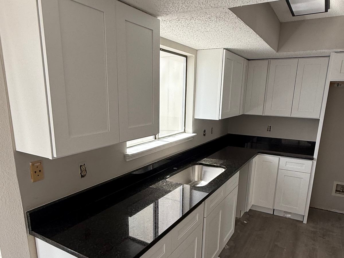 Cocina en L con gabinetes blancos estilo Shaker y encimera de granito negro con tarja bajo cubierta